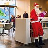 Weihnachtsmann stehend im Café Einstein. Er lehnt an einem Regal und liest in einem Buch mit der Aufschrift "Ho".