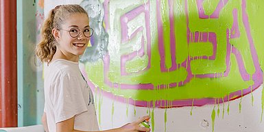 Mädchen mit Spraydose vor einer Wand mit Graffitis