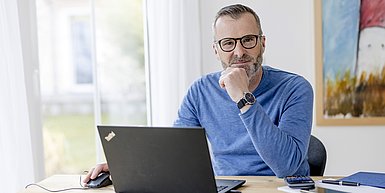 Mann mit Brille nachdenklich vor Laptop