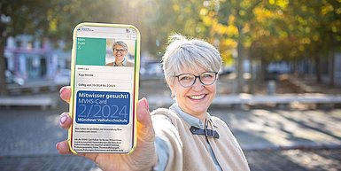 ältere Frau mit MVHS-Card 2/2024 auf dem Smartphone